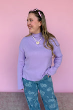Load image into Gallery viewer, Woman wearing a purple sweater and blue patterned pants against a pink background
