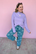 Load image into Gallery viewer, Woman wearing a purple sweater and blue floral pants against a pink background
