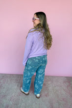 Load image into Gallery viewer, Woman wearing a lavender sweater and blue floral pants against a pink wall back view.

