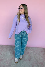 Load image into Gallery viewer, Woman wearing a purple sweater and blue floral pants against a pink background
