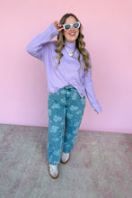 Load image into Gallery viewer, Woman wearing a light purple sweater and blue floral jeans against a pink wall.
