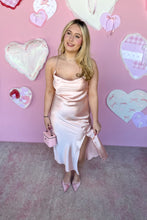 Load image into Gallery viewer, Woman in a pink satin dress standing against a pink wall with heart decorations.
