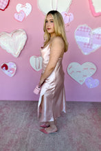 Load image into Gallery viewer, Woman in a pink satin outfit standing in front of a pink wall with heart decorations side with slit view.
