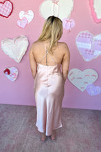 Load image into Gallery viewer, Woman wearing a pink satin dress with a heart-themed background back view
