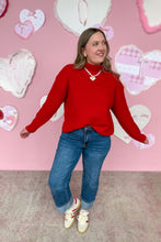 Load image into Gallery viewer, Person wearing a red sweater and blue jeans standing in front of a pink wall with heart decorations.
