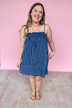 Load image into Gallery viewer, Girl in blue stripe spaghetti strap mini dress with pockets standing in front of a pink wall. 
