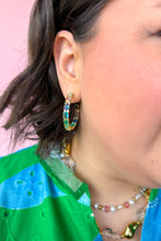 Load image into Gallery viewer, Close-up of a person wearing colorful hoop earrings with a pink background
