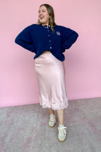 Load image into Gallery viewer, Woman wearing a blue sweater and pink skirt standing against a pink wall.
