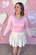 Load image into Gallery viewer, Woman wearing a pink top and white skirt in front of a pink heart-themed background
