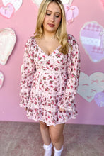 Load image into Gallery viewer, Woman wearing a pink floral dress against a pink background with heart shapes.
