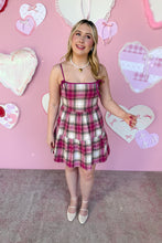 Load image into Gallery viewer, Woman in a plaid dress standing in front of a pink wall with heart decorations
