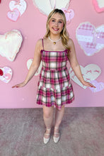 Load image into Gallery viewer, Woman in a plaid dress standing in front of a pink wall with heart decorations
