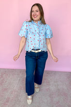 Load image into Gallery viewer, Girl wearing a blue top with red polkadots with puff sleeves and dark wash jeans standing in front of a pink background. 
