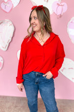 Load image into Gallery viewer, Woman wearing a red hoodie and blue jeans against a pink background with heart decorations.
