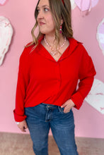 Load image into Gallery viewer, Woman wearing a red blouse and blue jeans against a pink background with heart decorations.
