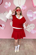 Load image into Gallery viewer, Person wearing a red skirt set with white collar and cuffs, holding a glass, against a pink wall with heart decorations.
