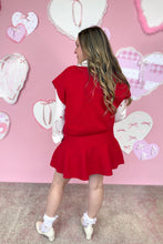 Load image into Gallery viewer, Woman in a red skirt set standing in front of a pink wall with heart decorations
