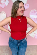Load image into Gallery viewer, Woman wearing a red sleeveless top and blue jeans against a pink background with heart shapes.
