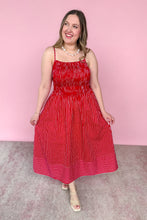 Load image into Gallery viewer, A woman modeling a red and white vertically striped midi dress with a smocked bodice, and beige strappy heels, set against a solid pink studio background.
