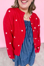 Load image into Gallery viewer, Person wearing a red cardigan with white star patterns and a blue striped dress against a pink background
