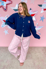 Load image into Gallery viewer, Person wearing a navy blue cardigan and pink pants with white polka dots against a pink wall with star decorations.
