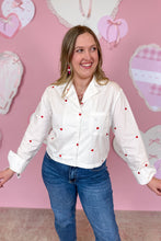Load image into Gallery viewer, Woman wearing a white shirt with red hearts in front of a pink wall with heart decorations
