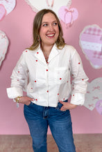 Load image into Gallery viewer, Woman wearing a white blouse with red hearts and blue jeans against a pink heart-shaped background
