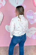 Load image into Gallery viewer, Woman wearing a white shirt with red hearts and blue jeans in front of a pink wall with heart decorations.
