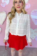 Load image into Gallery viewer, Woman wearing a white lace blouse and red skirt against a pink background with heart shapes.
