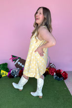 Load image into Gallery viewer, Girl wearing a yellow sleeveless polkadot shift dress with white boots standing in front of a pink background.
