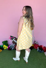 Load image into Gallery viewer, Girl wearing a yellow sleeveless polkadot shift dress with white boots standing in front of a pink background.
