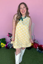 Load image into Gallery viewer, Girl wearing a yellow sleeveless polkadot shift dress with white boots standing in front of a pink background.
