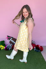 Load image into Gallery viewer, Girl wearing a yellow sleeveless polkadot shift dress with white boots standing in front of a pink background.
